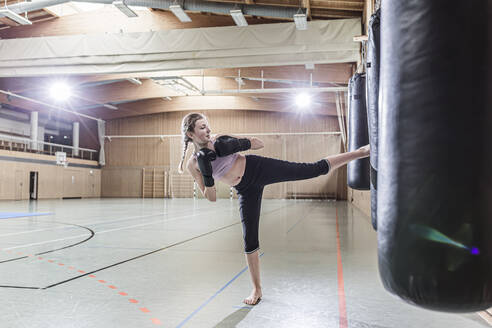 Weiblicher Kickboxer beim Training am Boxsack in der Sporthalle - STBF00491