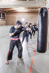 Coach and female boxers practising at punchbag in sports hall - STBF00496