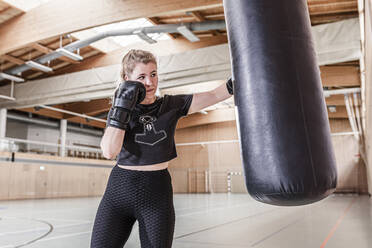 Female boxer practising at punchbag in sports hall - STBF00497