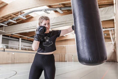 Weiblicher Boxer beim Training am Boxsack in der Sporthalle - STBF00497