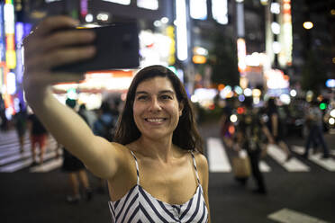 Junge Frau macht nachts ein Selfie in den Straßen von Shinjuku, Tokio, Japan - ABZF02633