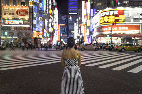 Junge Frau beim Nachdenken in der Nacht, Menschen überqueren die Shinjuku-Straße, Tokio, Japan - ABZF02634