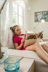 Mädchen sitzt auf der Couch und liest ein Buch - EGBF00365