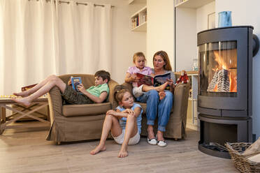 Familie entspannt und liest im Wohnzimmer am Kamin - EGBF00440