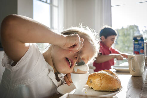 Girl eating a boiled egg at dining table - EGBF00442