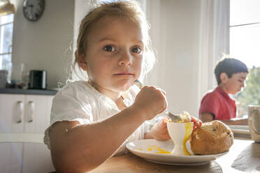 Porträt eines Mädchens, das am Esstisch ein gekochtes Ei isst - EGBF00444