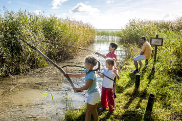 Children playing with wood sticks at water course, Darss, Mecklenburg-Western Pomerania, Germany - EGBF00461