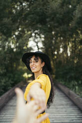 Young woman wearing a black hat and yellow dress and holding a hand - MTBF00058