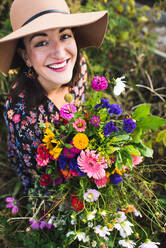 Glücklich lächelnde Frau in einem Garten mit frischen Blumen - CAVF65958