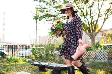 Glückliche Frau, die in einem städtischen Garten mit frischen Blumen spazieren geht - CAVF65969