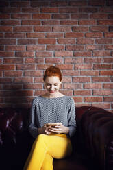 Glückliche Geschäftsfrau, die ein Smartphone benutzt, während sie auf der Couch in der Büro-Lobby sitzt - CAVF66127