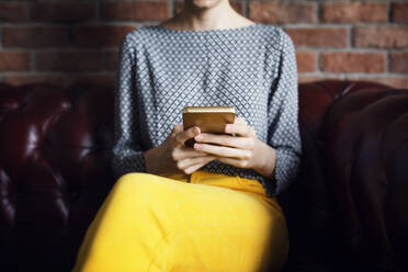 Midsection von Geschäftsfrau mit Smartphone auf der Couch im Büro Lobby - CAVF66128