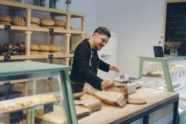 Happy owner holding paper bag while standing at counter in bakery - CAVF66135