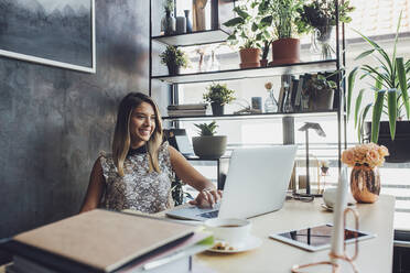 Smiling businesswoman working on laptop at home office - CAVF66139