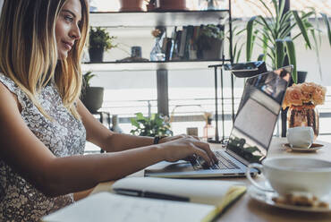 Businesswoman typing on laptop computer at table in home office - CAVF66140