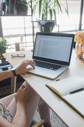 Cropped image of businesswoman using laptop computer at table in home office - CAVF66143