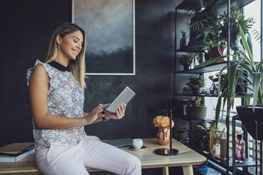 Lächelnde Geschäftsfrau, die einen Tablet-Computer benutzt, während sie auf einem Tisch im Heimbüro sitzt - CAVF66153