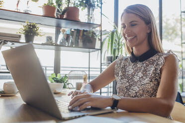Glückliche Geschäftsfrau, die einen Laptop benutzt, während sie an einem Tisch im Heimbüro sitzt - CAVF66164