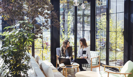 Businesswoman using laptop computer with colleague in cafe - CAVF66180