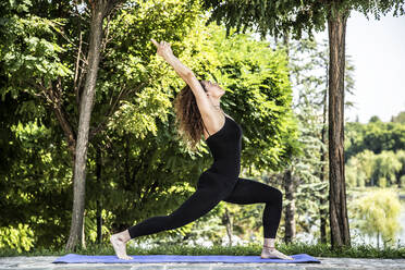 Confident woman practicing warrior pose in park - CAVF66219