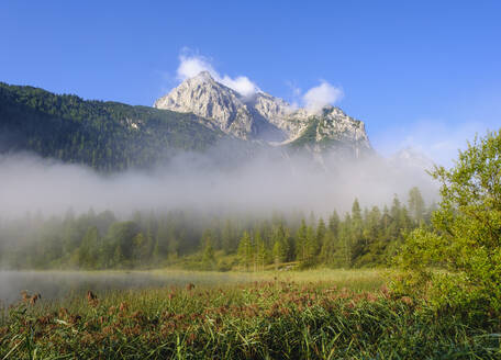 Deutschland, Bayern, Mittenwald, Dichter Nebel schwebt über dem Ferchensee mit Wettersteinspitzen im Hintergrund - SIEF09225