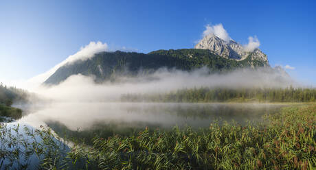 Deutschland, Bayern, Mittenwald, Dichter Nebel schwebt über dem Ferchensee mit Wettersteinspitzen im Hintergrund - SIEF09227