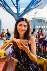 Thailändische Frau mit Telefon in der Rooftop Bar - CAVF66256