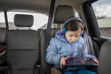 Vorderansicht eines kleinen Kindes in einem Autositz, das einen Tablet-Bildschirm betrachtet - CAVF66281
