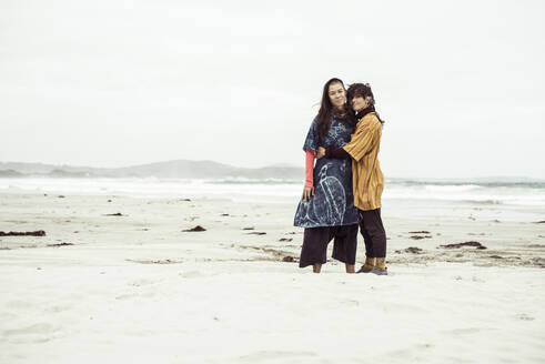 Same sex lesbian couple hug on wild remote beach adventure in the wind - CAVF66310