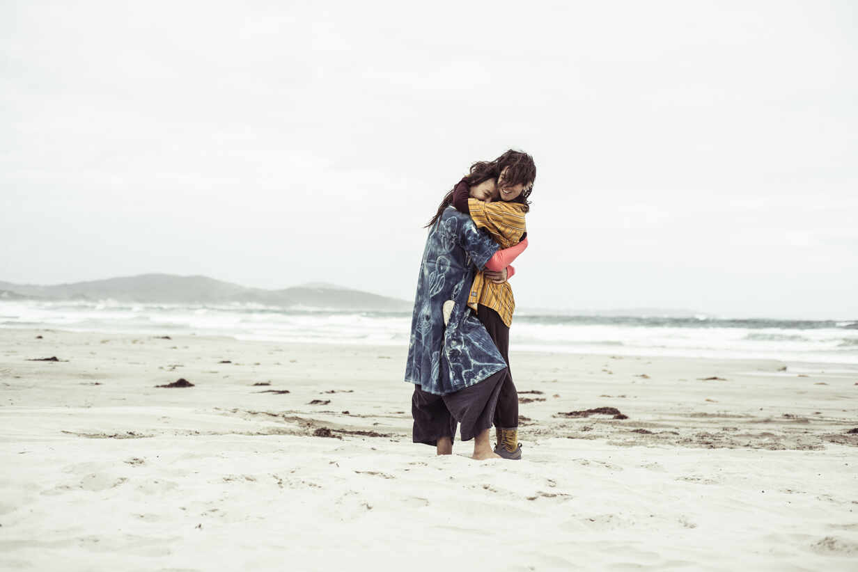 Same sex lesbian couple hug on wild remote beach adventure in the wind  stock photo