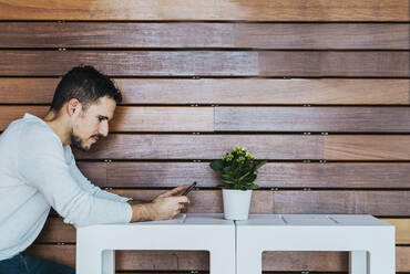 Seitenansicht eines Mannes, der in einem Café ein Mobiltelefon benutzt - CAVF66316