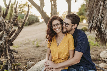 Mid adult couple embracing on rock smiling as they hug close - CAVF66332