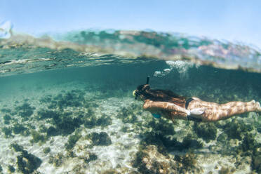 Side view of woman in bikini snorkeling underwater - CAVF66524