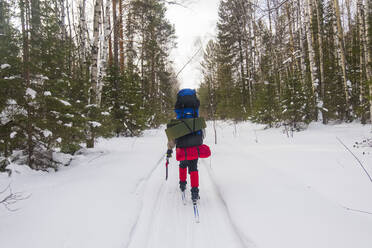 Rear view of man with backpacks skiing on snow covered field - CAVF66552