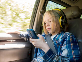 Junge benutzt Mobiltelefon beim Musikhören im Auto - CAVF66626