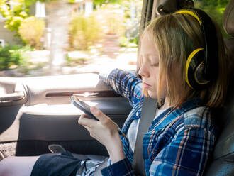 Junge schaut auf sein Mobiltelefon, während er im Auto Musik hört - CAVF66627