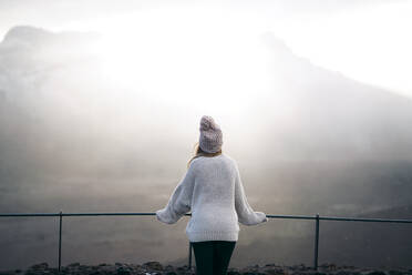 Rear view of woman standing by railing at observation point against mountain - CAVF66635