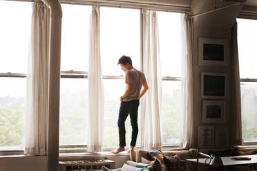 Thoughtful man standing on window sill at home - CAVF66653
