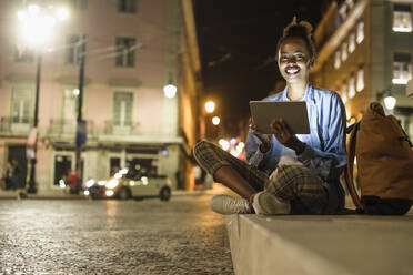 Porträt einer glücklichen jungen Frau mit digitalem Tablet in der Stadt bei Nacht, Lissabon, Portugal - UUF19130