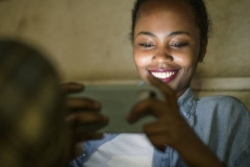 Porträt einer glücklichen jungen Frau, die bei Nacht ein Smartphone benutzt, Lissabon, Portugal - UUF19139