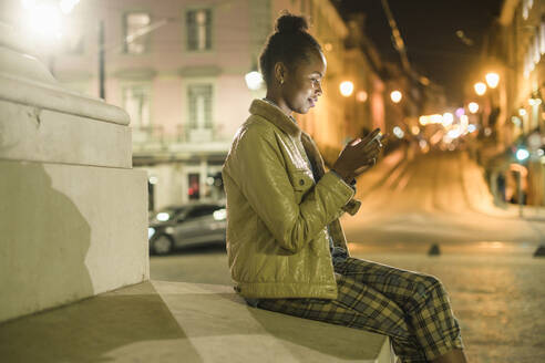 Junge Frau mit Smartphone in der nächtlichen Stadt, Lissabon, Portugal - UUF19158
