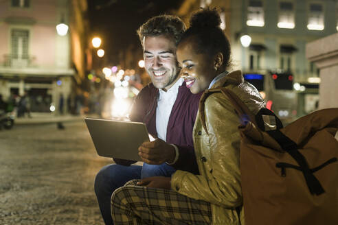 Porträt eines glücklichen jungen Paares bei der Nutzung eines digitalen Tablets in der nächtlichen Stadt, Lissabon, Portugal - UUF19161