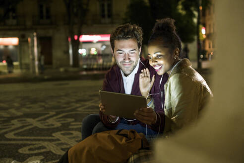 Porträt eines lächelnden jungen Paares, das sich Kopfhörer teilt und auf ein digitales Tablet schaut, Lissabon, Portugal - UUF19164
