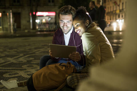 Porträt eines glücklichen jungen Paares, das sich Kopfhörer teilt und auf ein digitales Tablet schaut, Lissabon, Portugal, lizenzfreies Stockfoto