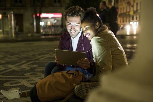 Porträt eines glücklichen jungen Paares, das sich Kopfhörer teilt und auf ein digitales Tablet schaut, Lissabon, Portugal - UUF19165