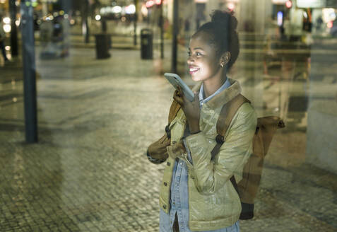 Lächelnde junge Frau am Telefon in der Stadt bei Nacht, Lissabon, Portugal - UUF19171