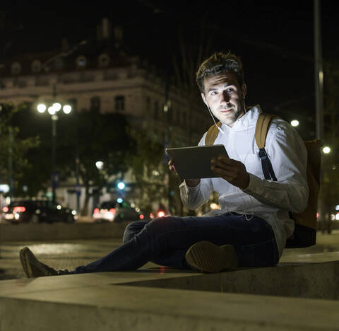 Porträt eines jungen Mannes mit digitalem Tablet und Kopfhörern in der nächtlichen Stadt, Lissabon, Portugal, lizenzfreies Stockfoto