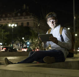 Porträt eines jungen Mannes mit digitalem Tablet und Kopfhörern in der nächtlichen Stadt, Lissabon, Portugal - UUF19190