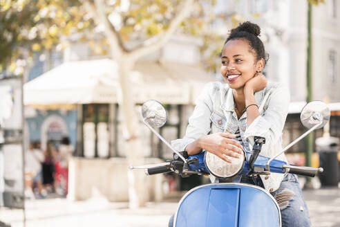 Glückliche junge Frau mit Motorroller in der Stadt, Lissabon, Portugal - UUF19199