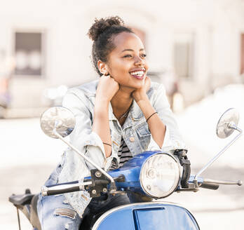 Glückliche junge Frau mit Motorroller in der Stadt, Lissabon, Portugal - UUF19201